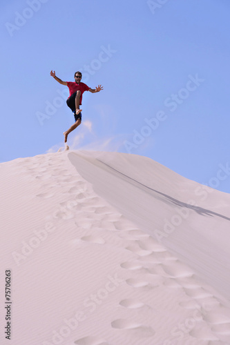 Young on top of a dune,jumping on the sand