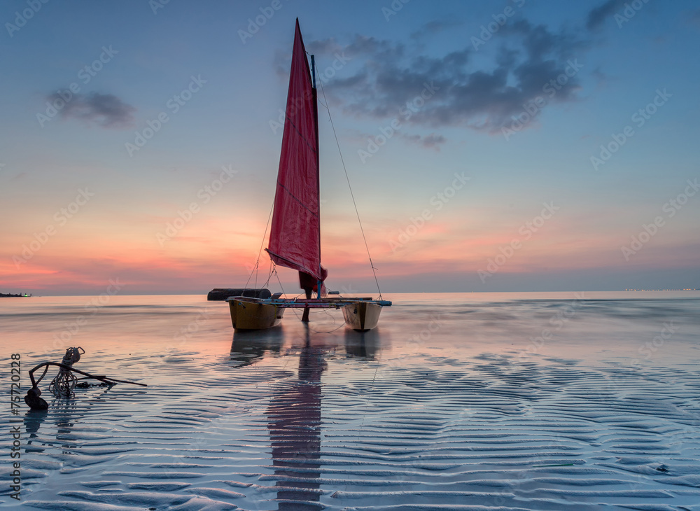 Naklejka premium Red sailboat on the beach with a beautiful sunset