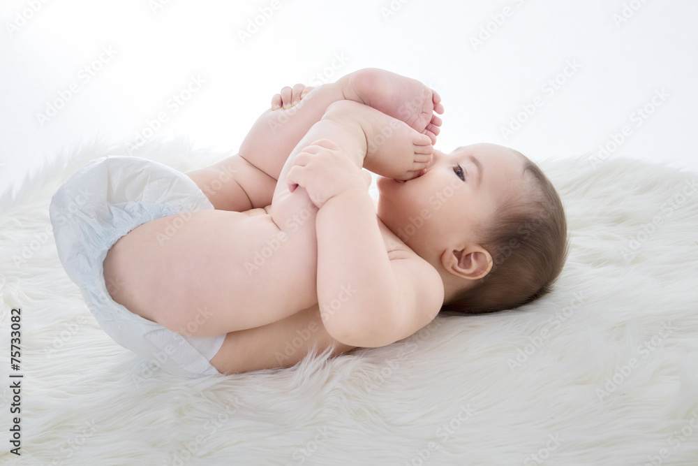 Kleines Mädchen liegt auf Schafsfell und spielt mit den Füssen Kleines Mädchen liegt auf Schafsfell und spielt mit den Füssen