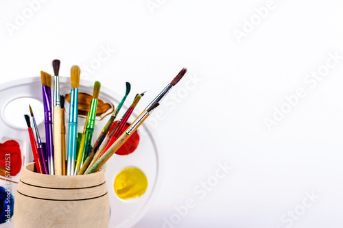 brushes in wooden bucket and paint palette, isolated