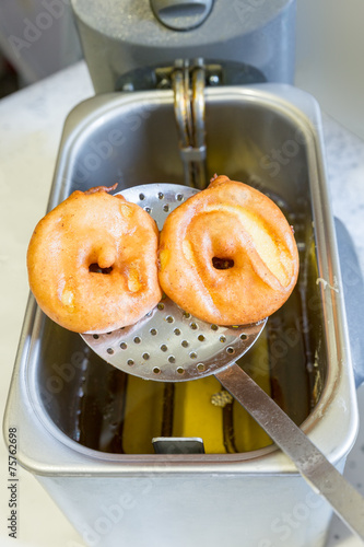 Apple turnovers on spoon above frying oil photo