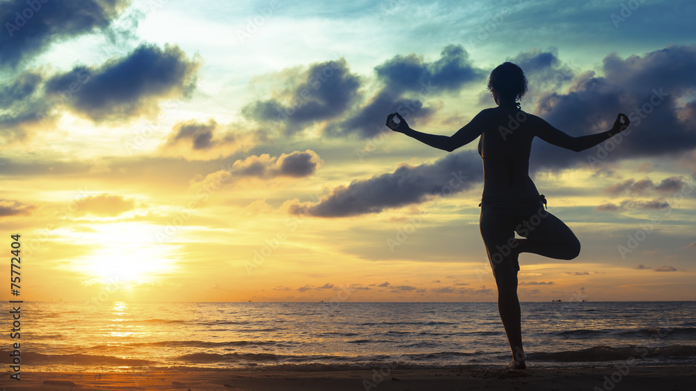 Yoga woman meditation on ocean coast during an amazing sunset.