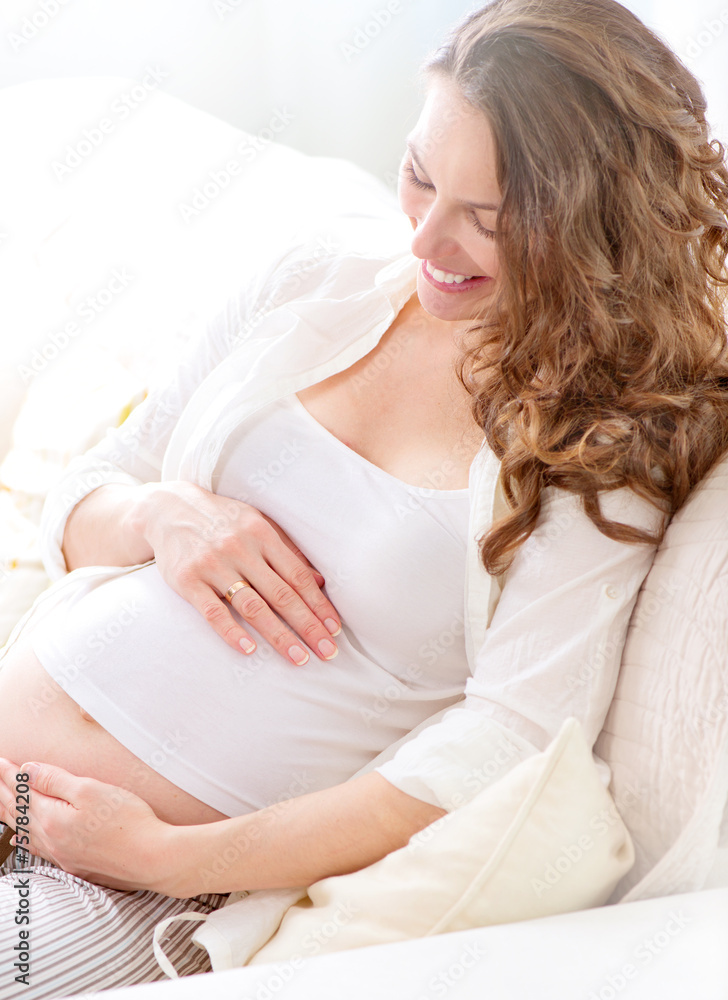 Pregnant smiling woman sitting on a sofa and caressing her belly Pregnant smiling woman sitting on a sofa and caressing her belly