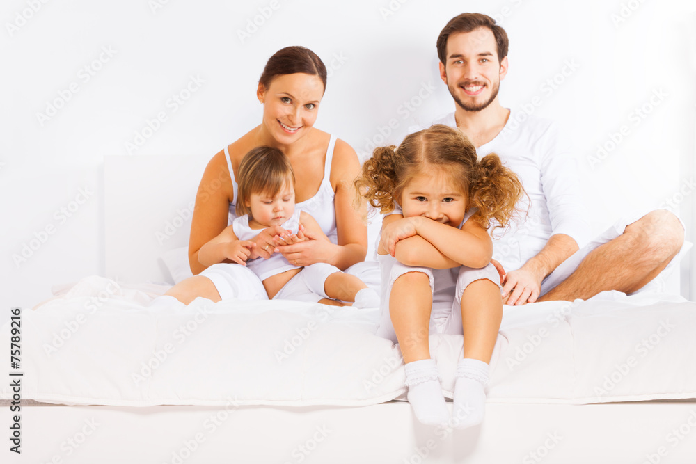 Family sitting on white bed in pajamas together