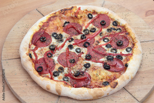Closeup of pizza with salami, peperoni, black olives and pepper.