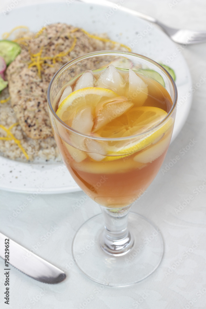 Iced tea with lemon next to plate full of food. Iced tea with lemon next to plate full of food.