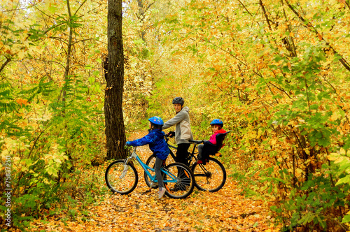 Family on bikes in autumn park, father and kids cycling