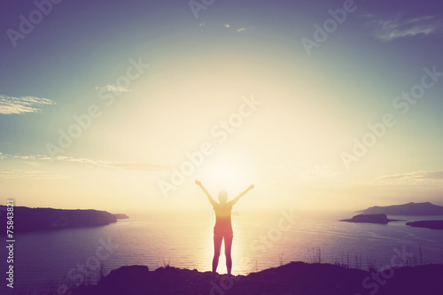Happy woman with hands up over sea and islands at sunset