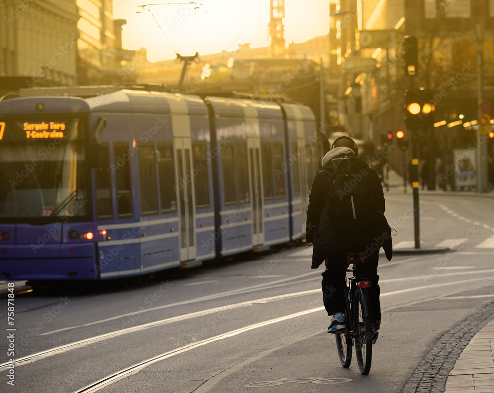 Bike commuter and tram in sunlit city - obrazy, fototapety, plakaty 