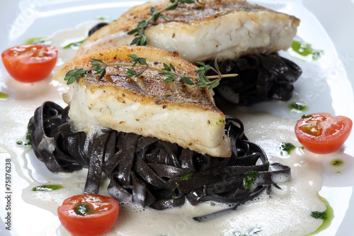 Auf der Haut gebratene Fischfilets auf schwarzen Bandnudeln mit Soßenschäumchen photo