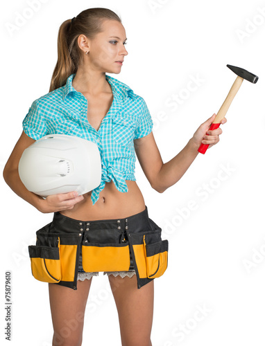 Pretty girl in tool belt holding white helmet and hammer