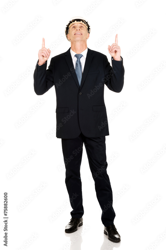 Smiling businessman with hard hat pointing up Smiling businessman with hard hat pointing up