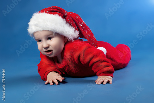 Christmas baby boy in Santa's hat is lying on blue plaid