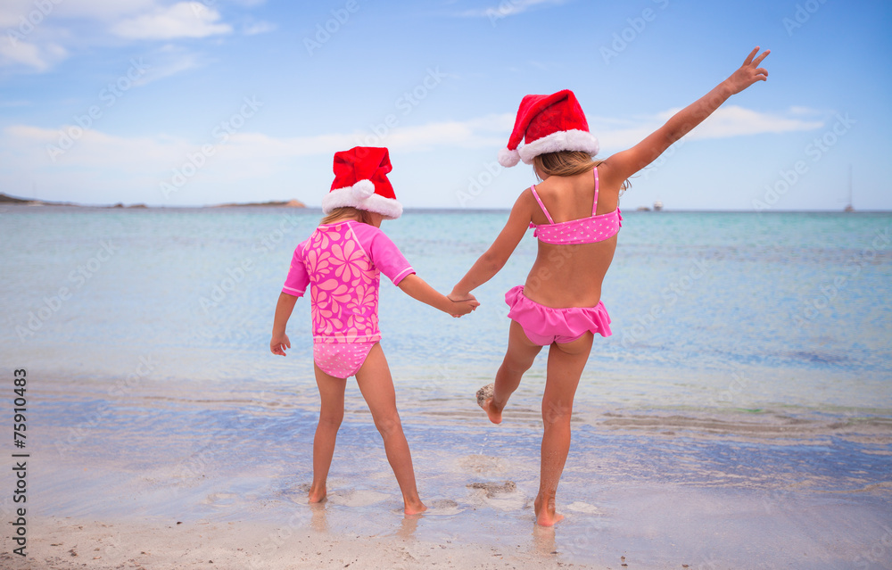 Little adorable girls in Santa hats during beach vacation Little adorable girls in Santa hats during beach vacation