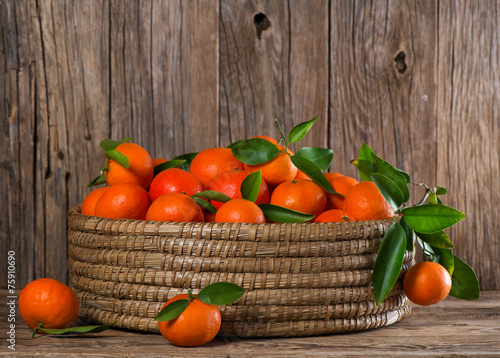 Tangerines or mandarins with leaves in a great  basket on a wood