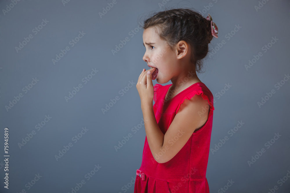 Teen girl fingers in his mouth red dress on a gray backgrou
