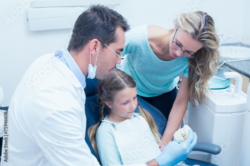Dentist with assistant teaching girl how to brush teeth