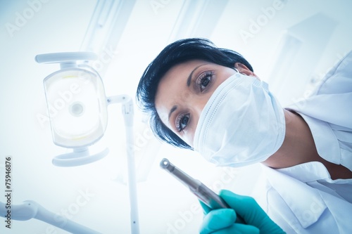 Female dentist in surgical mask holding dental drill photo