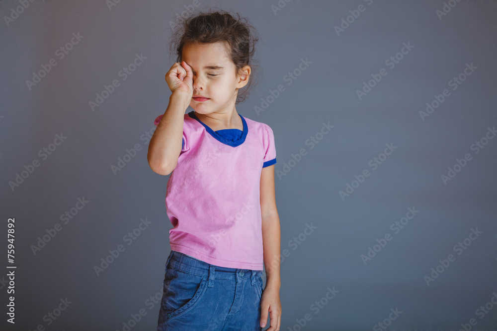 the girl child is tired rubs his eyes on gray background the girl child is tired rubs his eyes on gray background