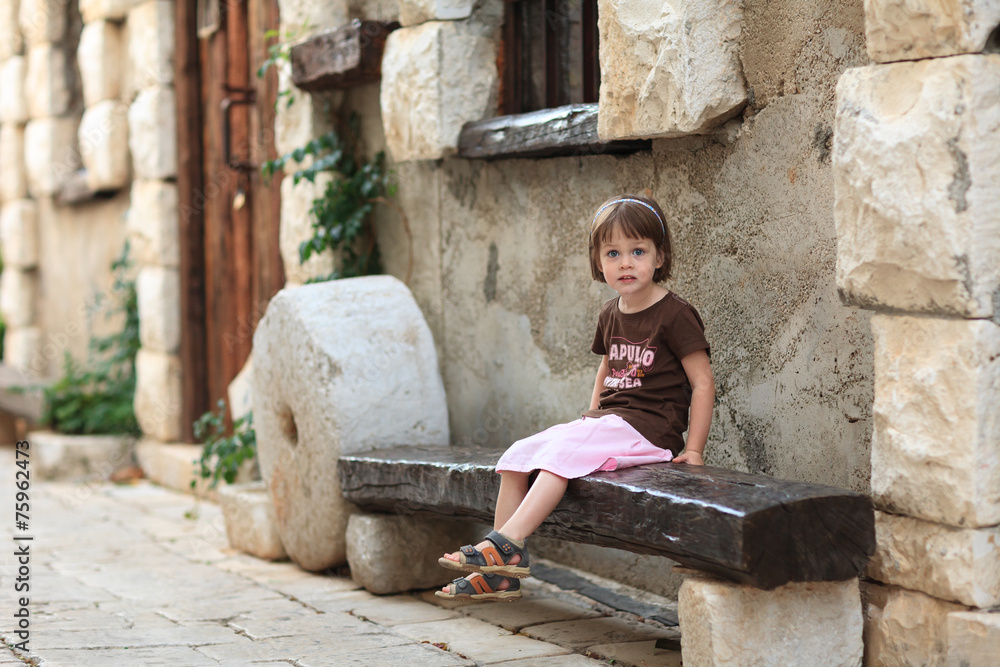 Little girl sitting on an old wooden bench