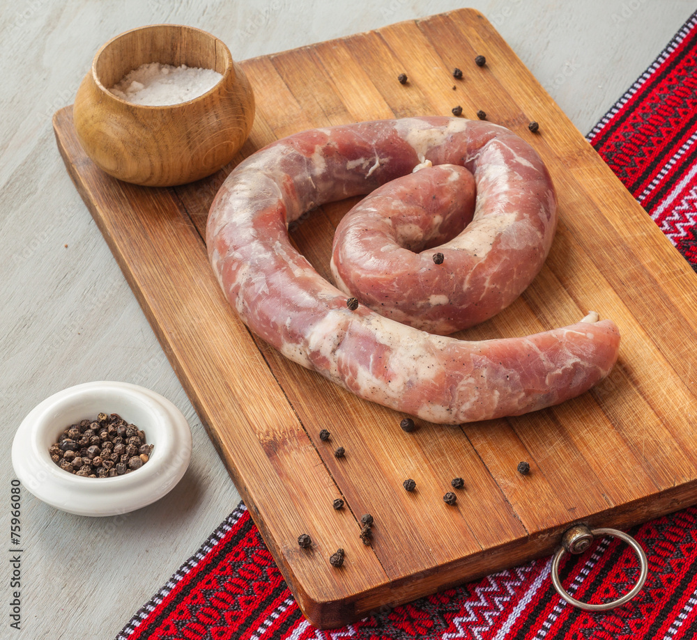 Ring of raw sausage on a cutting board with pepper Ring of raw sausage on a cutting board with pepper