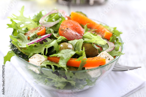 Greek salad in glass dish on napkin and color wooden background