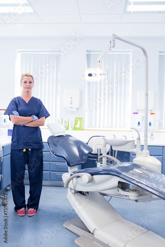 Dentist in blue scrubs standing with arms crossed