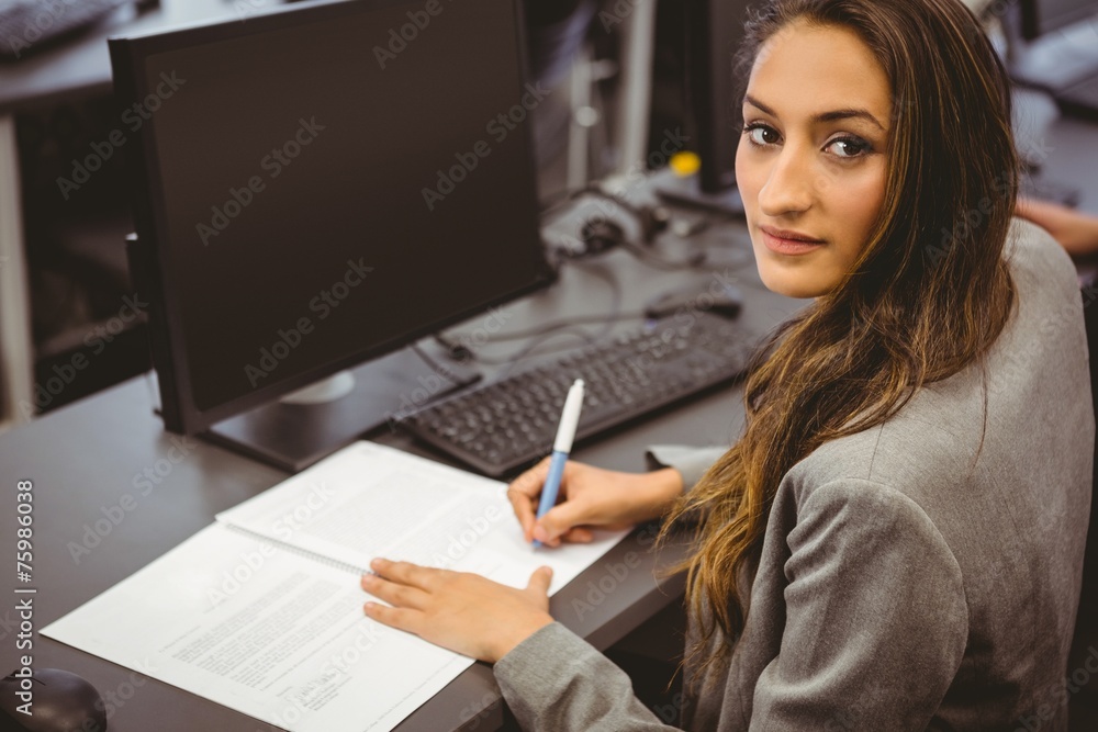 Smiling student sitting at desk writing on notepad Smiling student sitting at desk writing on notepad