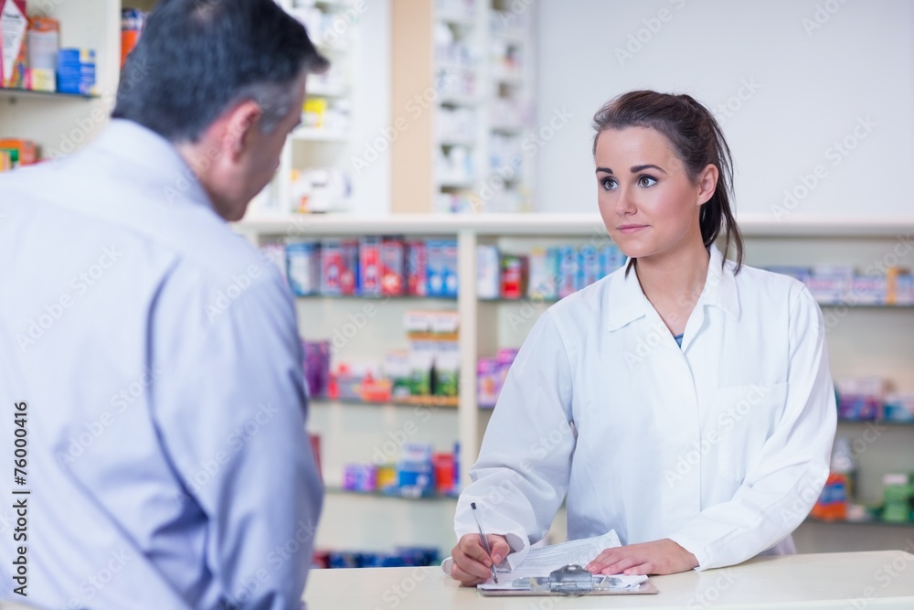 Trainee writing prescription in front of a customer Trainee writing prescription in front of a customer