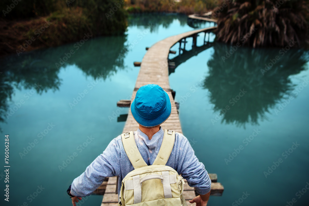 tourist man walking across wooden bridge over glossy blue lake tourist man walking across wooden bridge over glossy blue lake