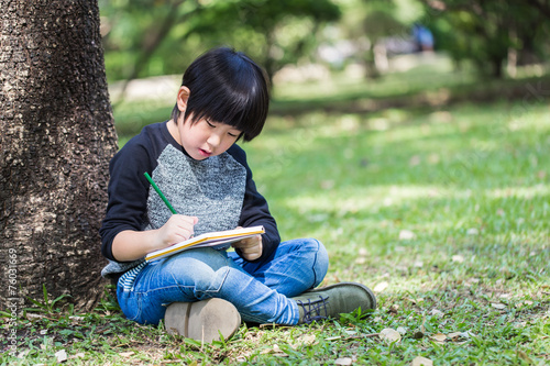 Little asian boy writing book in the park