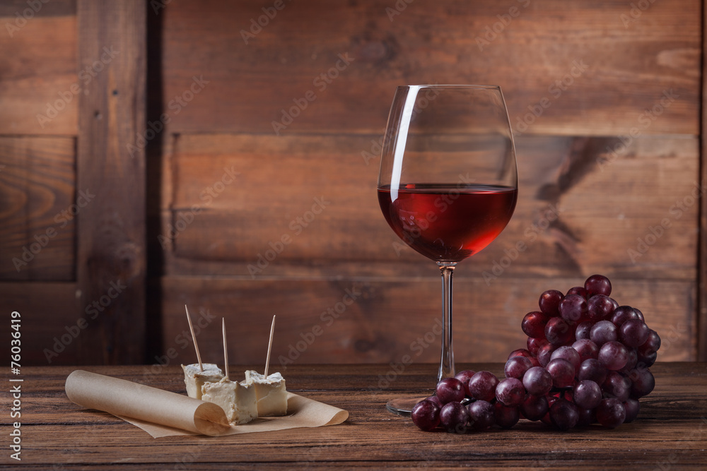 Red wine in glass with grape and cheese on wood