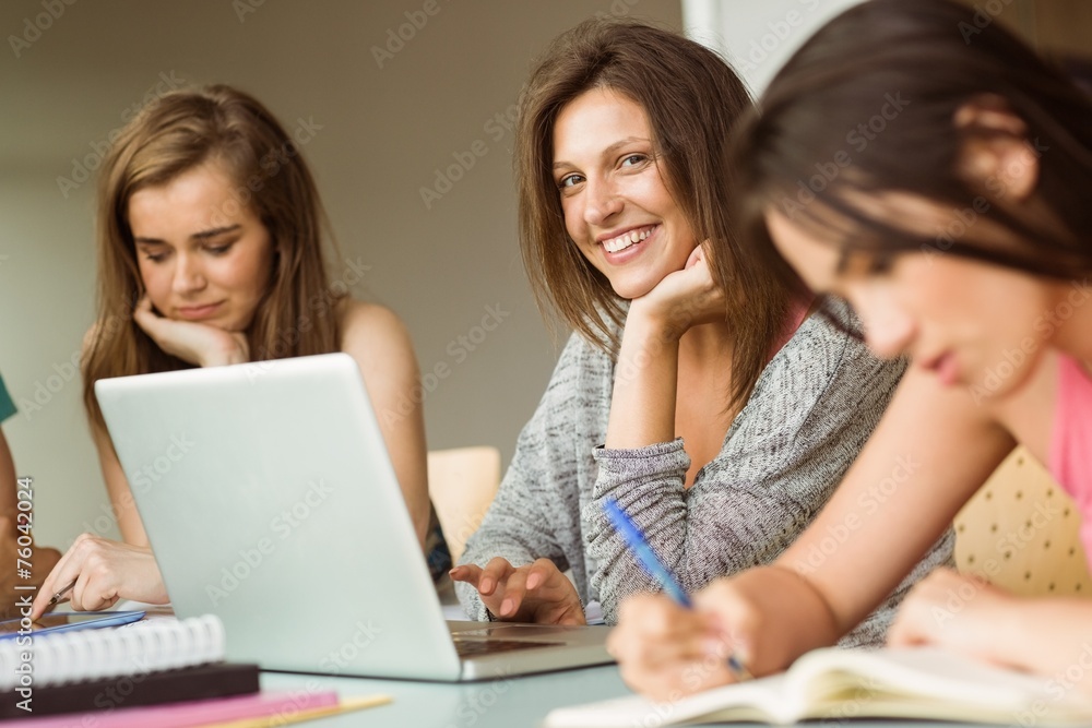 Smiling friends sitting studying and using laptop