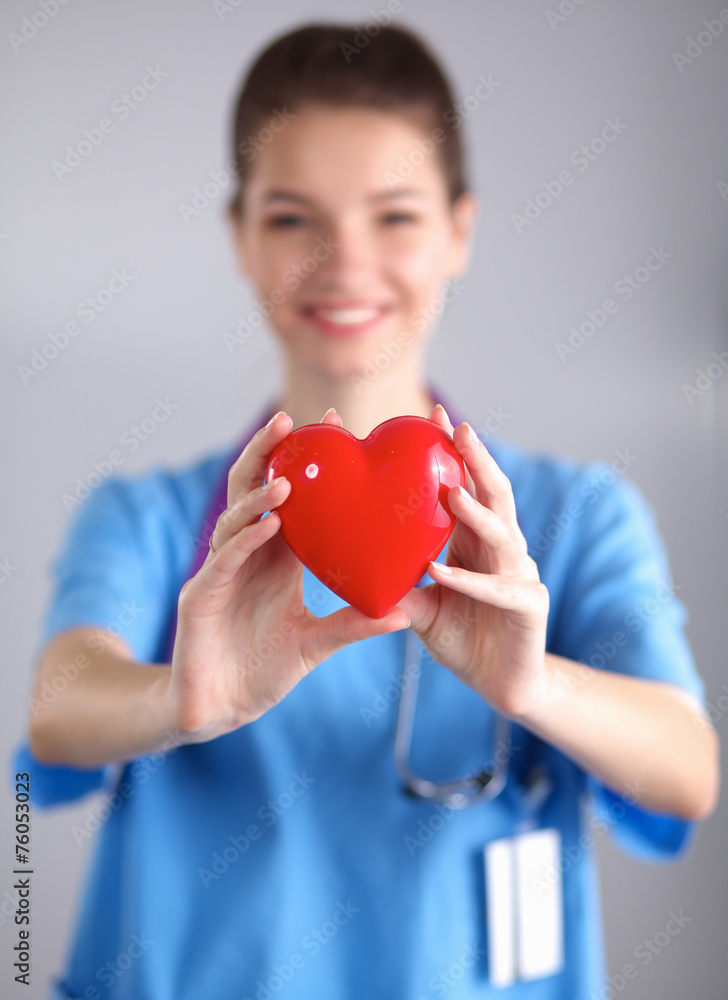 Young woman doctor holding a red heart, standing on gray