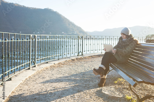 girl uses her tablet on a bench, in the background the lake
