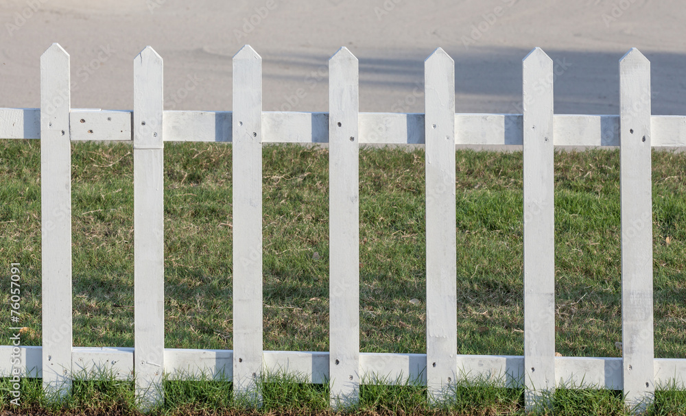 Close up the white wooden fence nearby pathway and green grass. Close up the white wooden fence nearby pathway and green grass.
