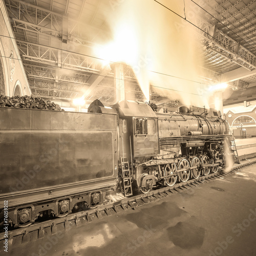 Steam train arrives to the station at night time.