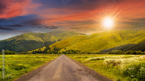 abandoned road through meadows in mountain at sunset
