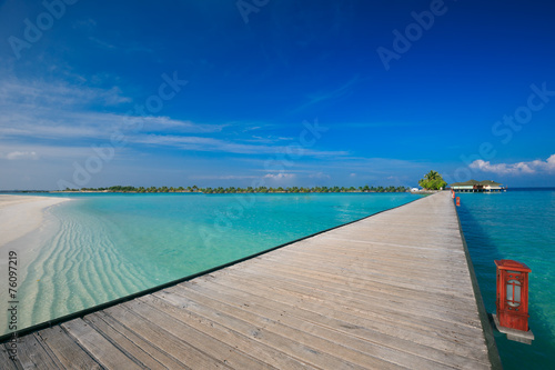 Bridge leading to overwater bungalow in blue lagoon around tropi photo