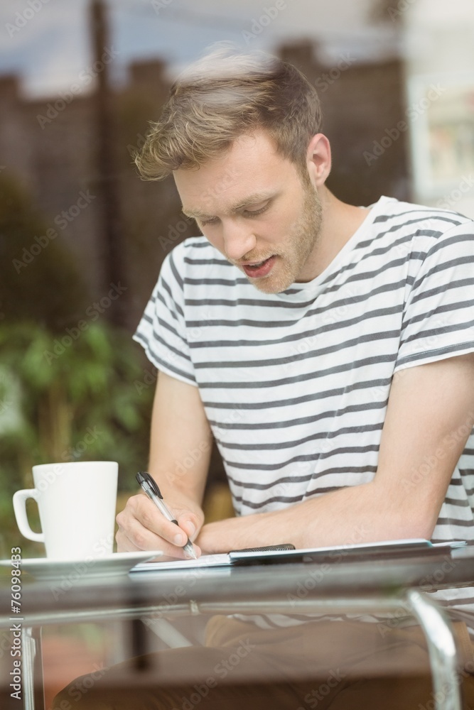 Smiling student sitting with a hot drink and writing on notepad