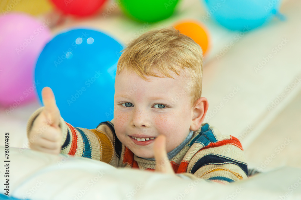 Obraz premium A little boy lying on the floor surrounded by colorful balloons