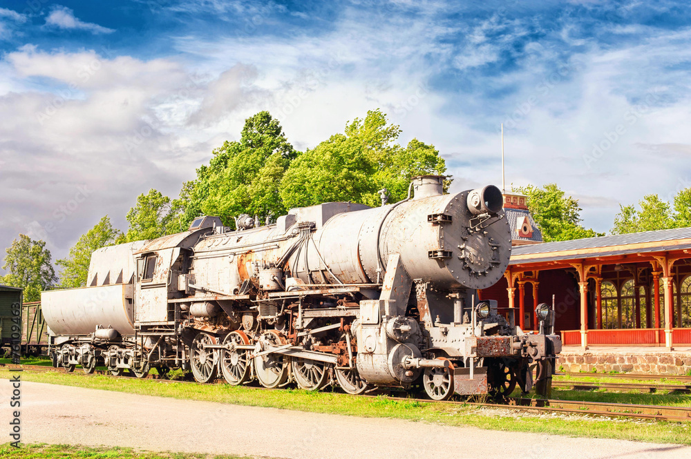 Old rustic steam locomotive on station platform. Cloudy sky back Old rustic steam locomotive on station platform. Cloudy sky back
