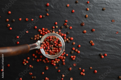 Cooking spoon with pink peppercorns on dark, stone background