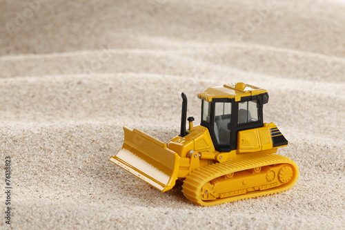 Heavy crawler toy bulldozer on sand dune
