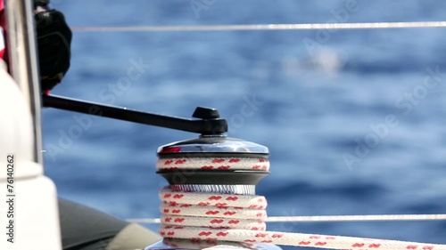 Man pulling ropes, winding sheets around winches. Sailing.