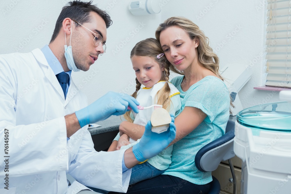 Fototapeta premium Dentist with assistant teaching girl how to brush teeth