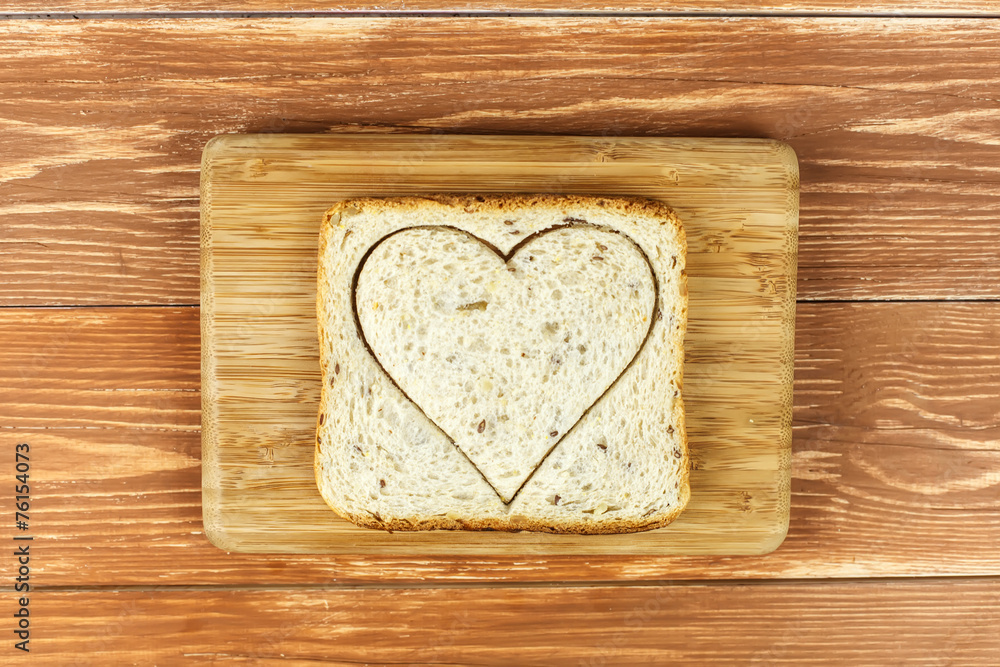 Slice of cereal toast bread with cut out heart shape on wooden Slice of cereal toast bread with cut out heart shape on wooden