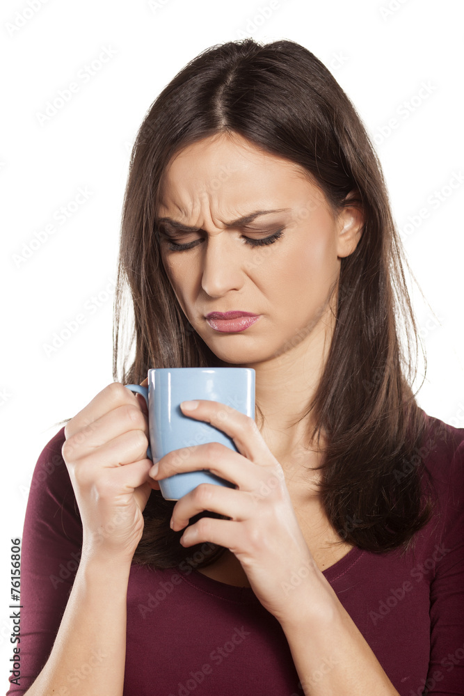 scowling young woman is disgusted by the smell of her drink scowling young woman is disgusted by the smell of her drink