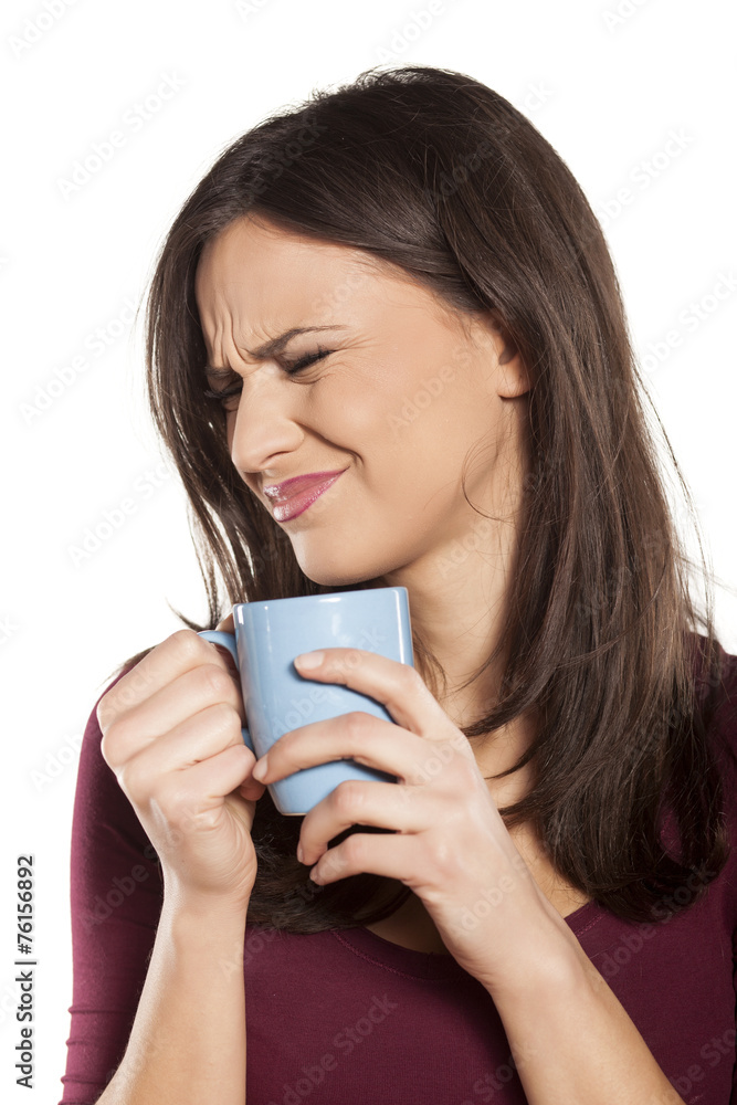 scowling young woman is disgusted by the smell of her drink scowling young woman is disgusted by the smell of her drink