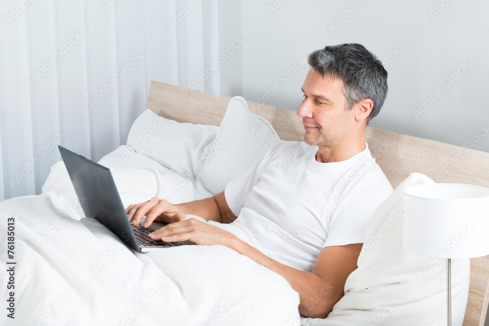 Man Relaxing On Bed Using Laptop Man Relaxing On Bed Using Laptop